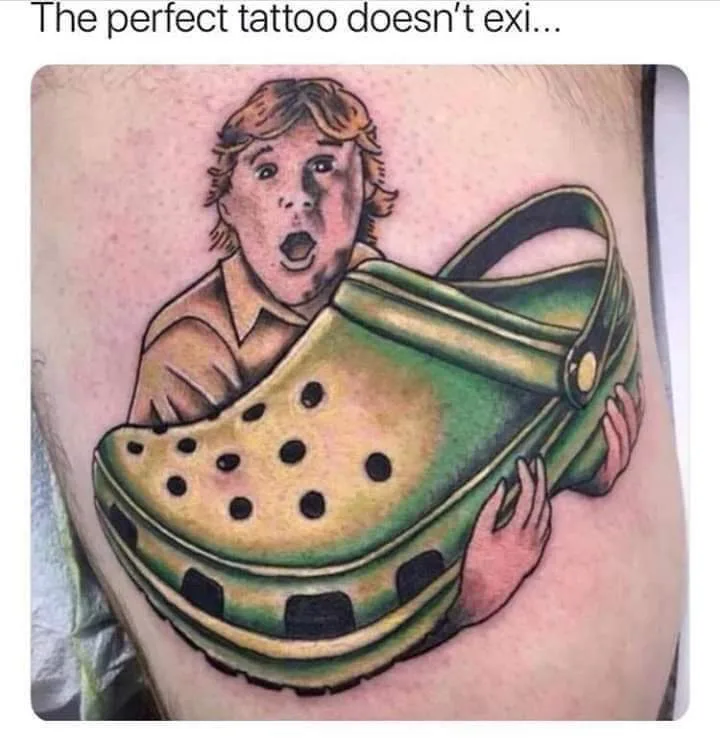 A tattoo on human skin depicts a cartoonish boy with wide eyes and an open mouth, appearing shocked or surprised, as he is…
