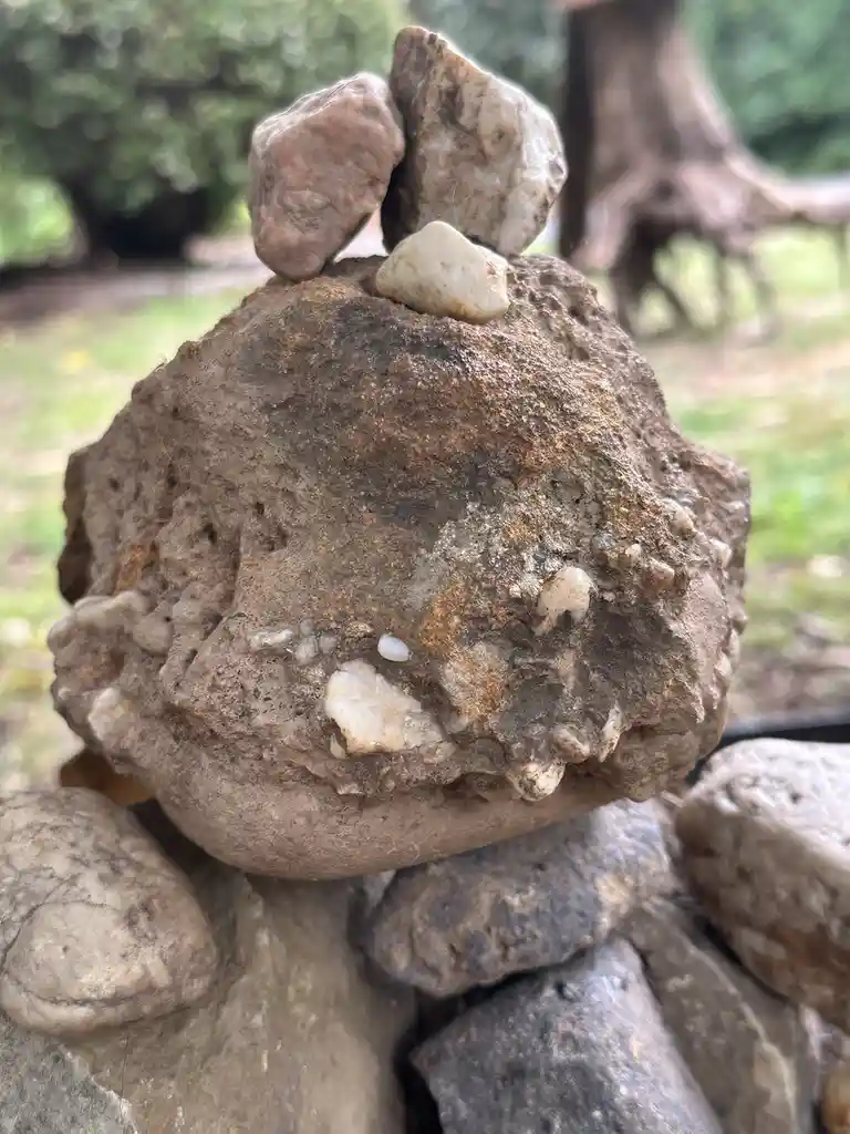 A close-up photo of a carefully balanced rock sculpture outdoors, where the central rock has two smaller rocks perched on…