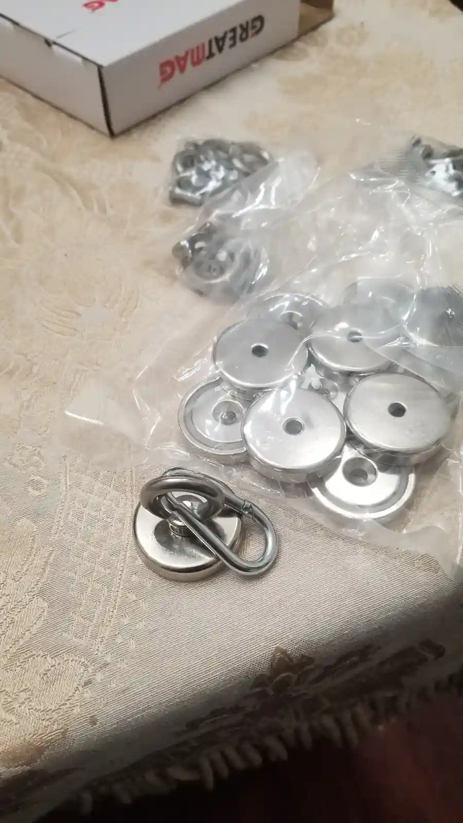 A close-up photo shows a collection of small, round, silver-colored magnetic discs in clear plastic packaging, with one disc…