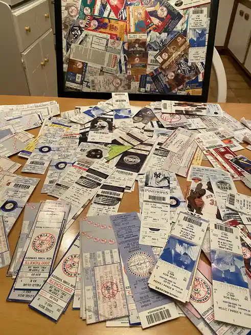 A wooden table is covered with a large pile of baseball and basketball game tickets, mostly from the New York Yankees and…
