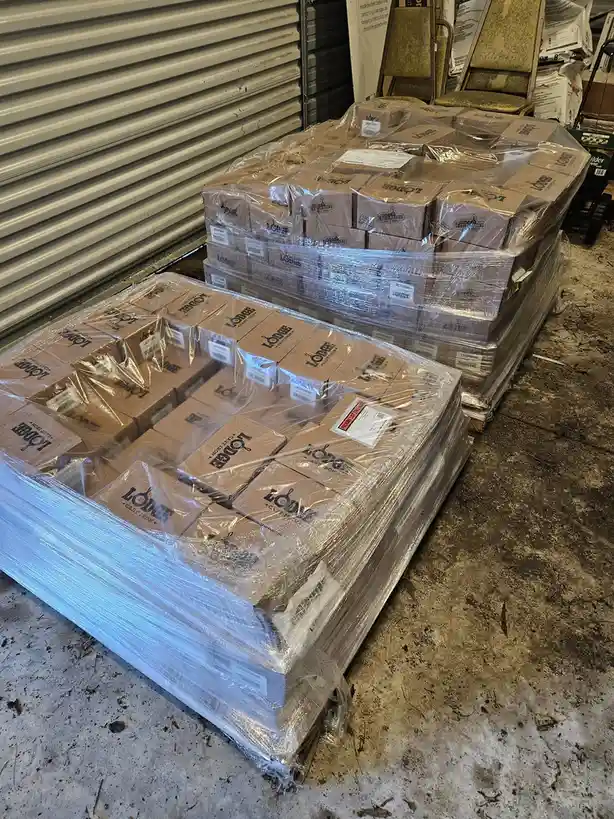 Two large pallets wrapped in plastic wrap are stacked in a warehouse, each holding many cardboard boxes labeled 'LODGE CAST…