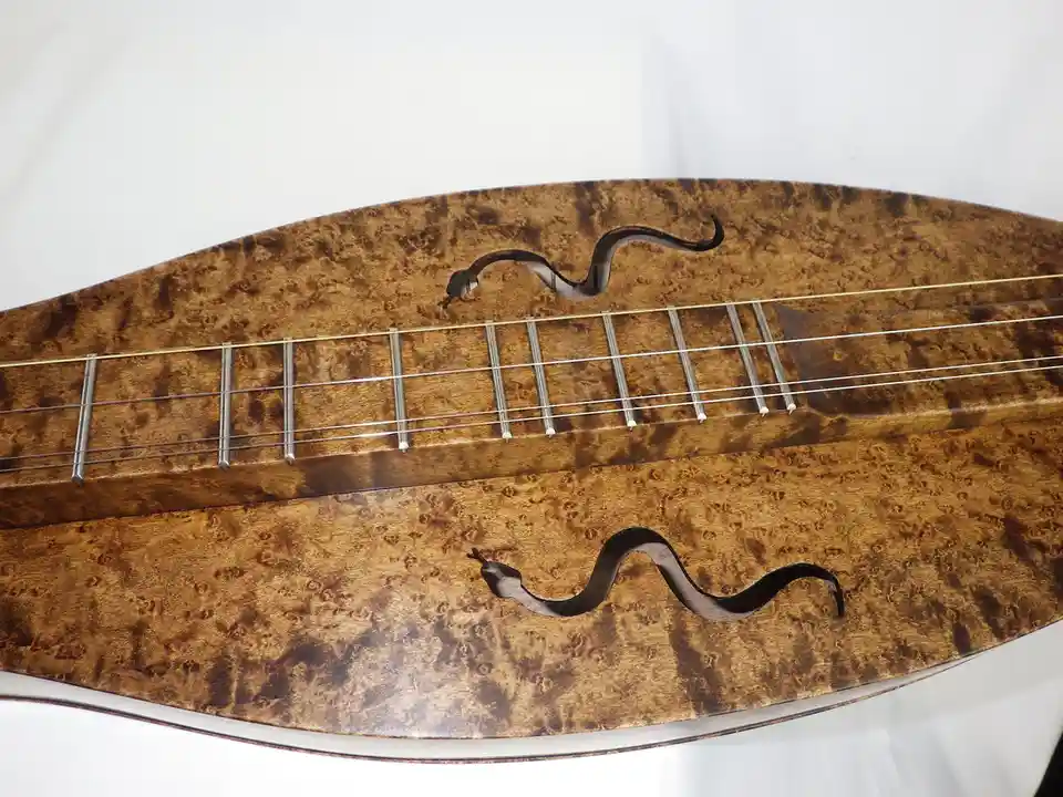 A close-up of a stringed musical instrument with a highly figured wood body, showing two f-holes shaped like snakes, one…
