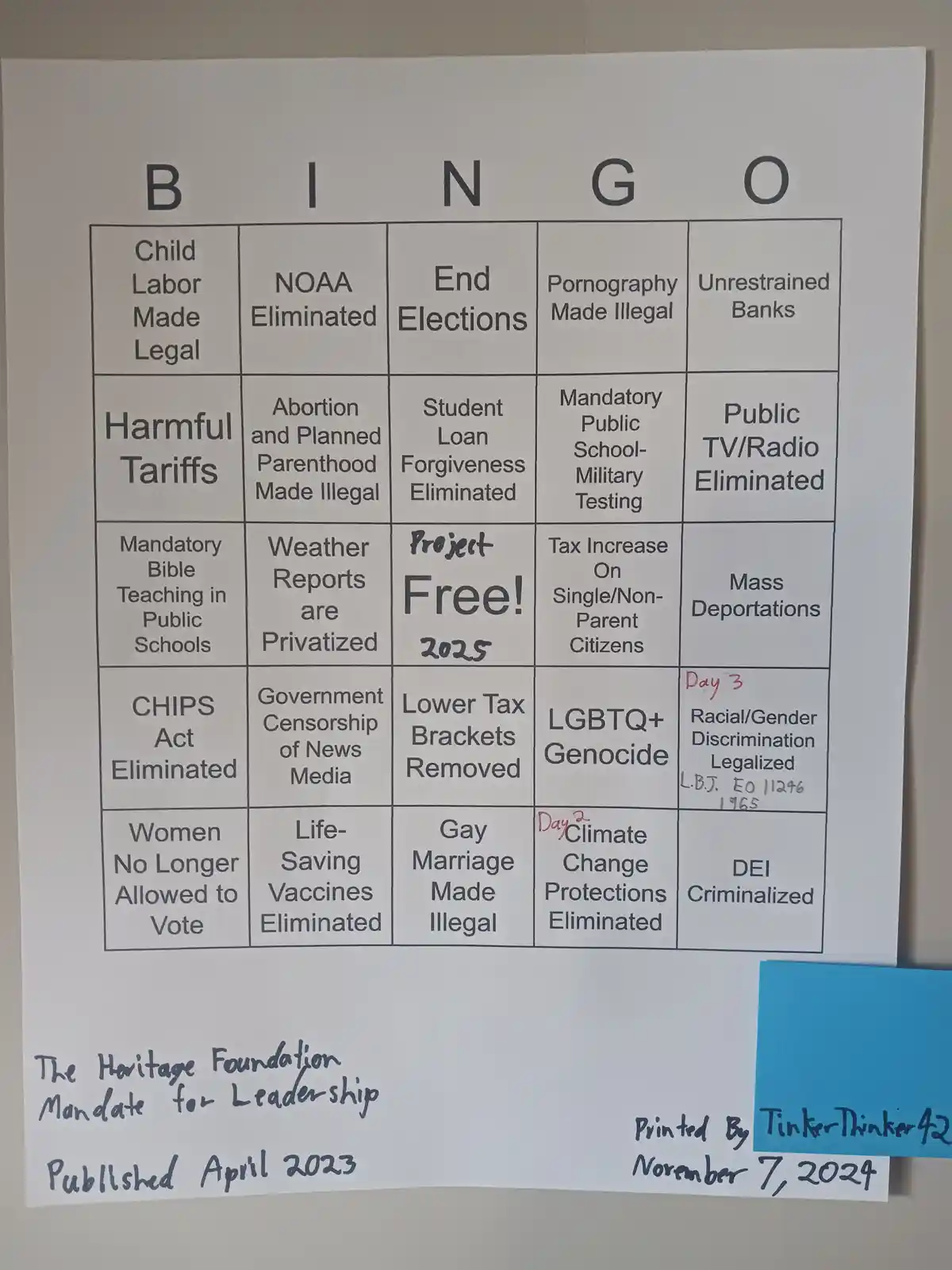 A printed bingo card with extreme political and social policy squares like 'Child Labor Made Legal' and 'LGBTQ+ Genocide'…
