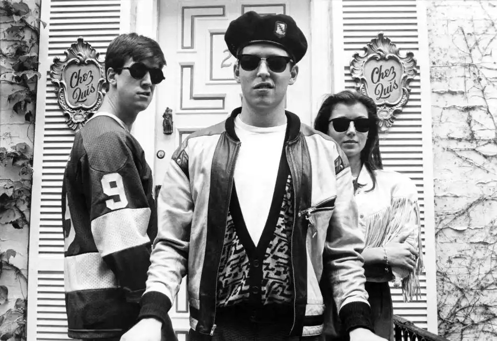 A black-and-white photo shows three people standing in front of a door with ornate 'Chez Quis' signs on either side. The…