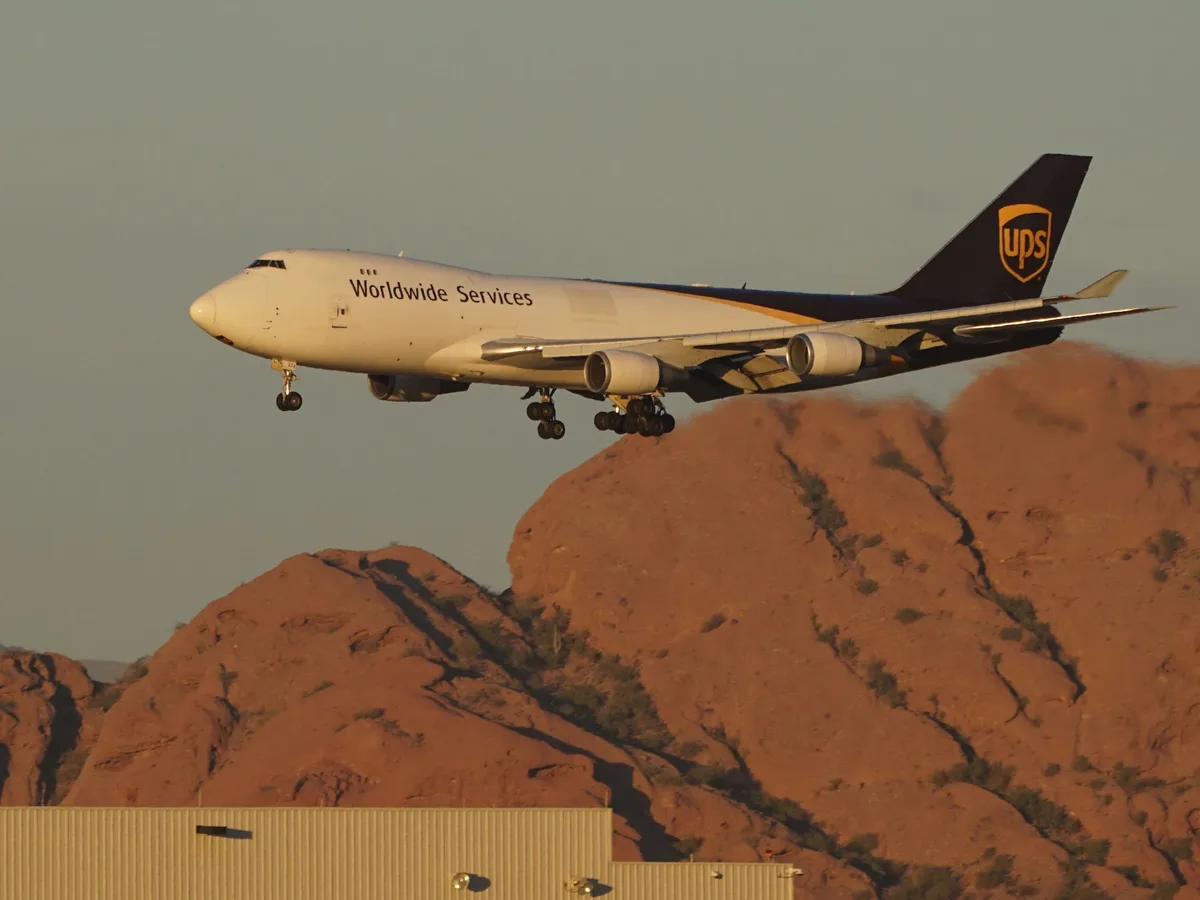 A UPS cargo plane, with 'Worldwide Services' written on its fuselage and the UPS logo on its tail, is captured in mid-flight…