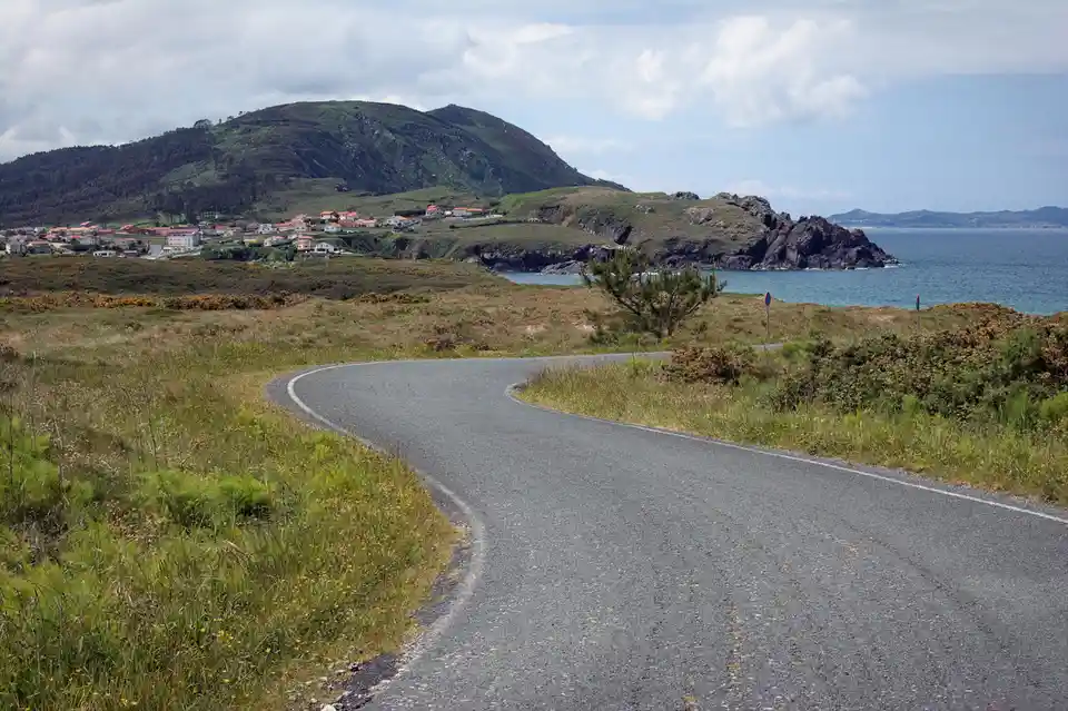 A scenic coastal road curves through grassy hills toward a village and the ocean, with overlaid text reading 'i'm not lost…
