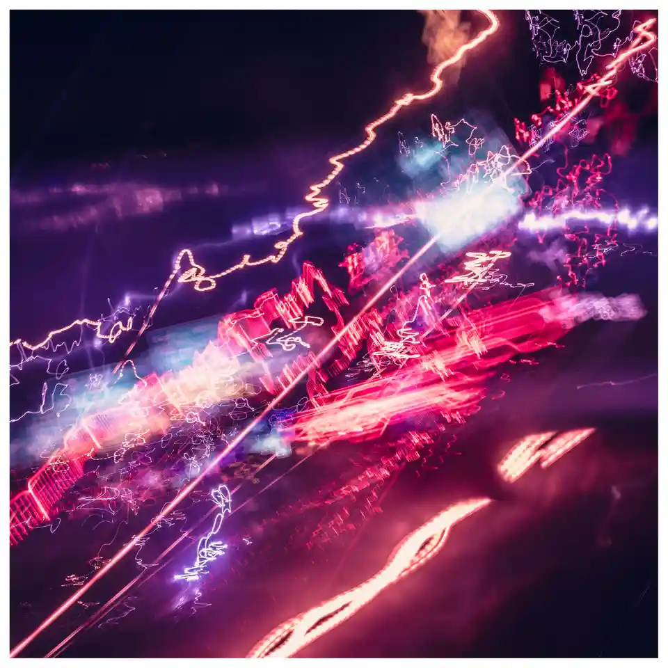 A long-exposure night photograph shows abstract streaks of red, pink, and purple light against a dark background, resembling…