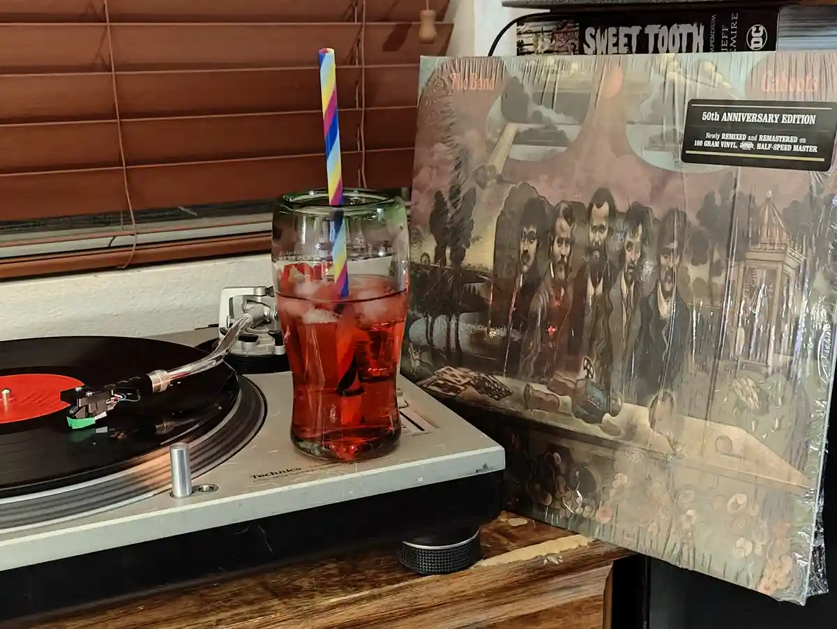 A Technics turntable plays a red vinyl record while a glass of red drink with a colorful striped straw sits on top. Beside…