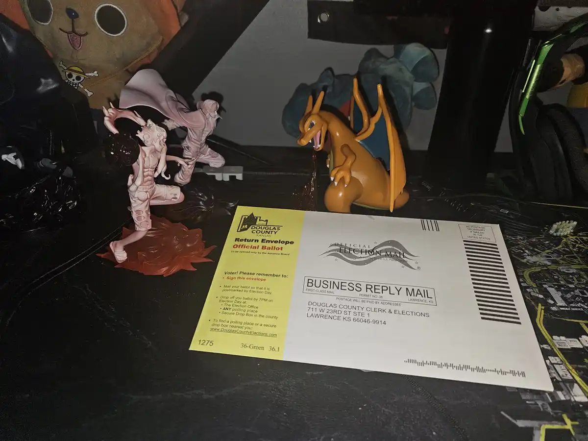 A Douglas County, Kansas official election mail ballot envelope lies on a desk surrounded by anime and Pokémon figurines…