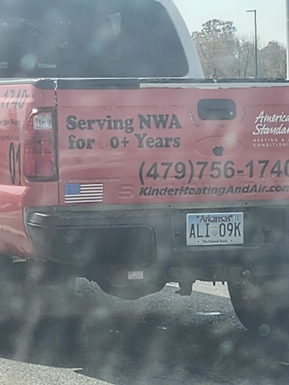 The rear of a red pickup truck with faded business decals, including 'Serving NWA for 0+ Years', a phone number, and…
