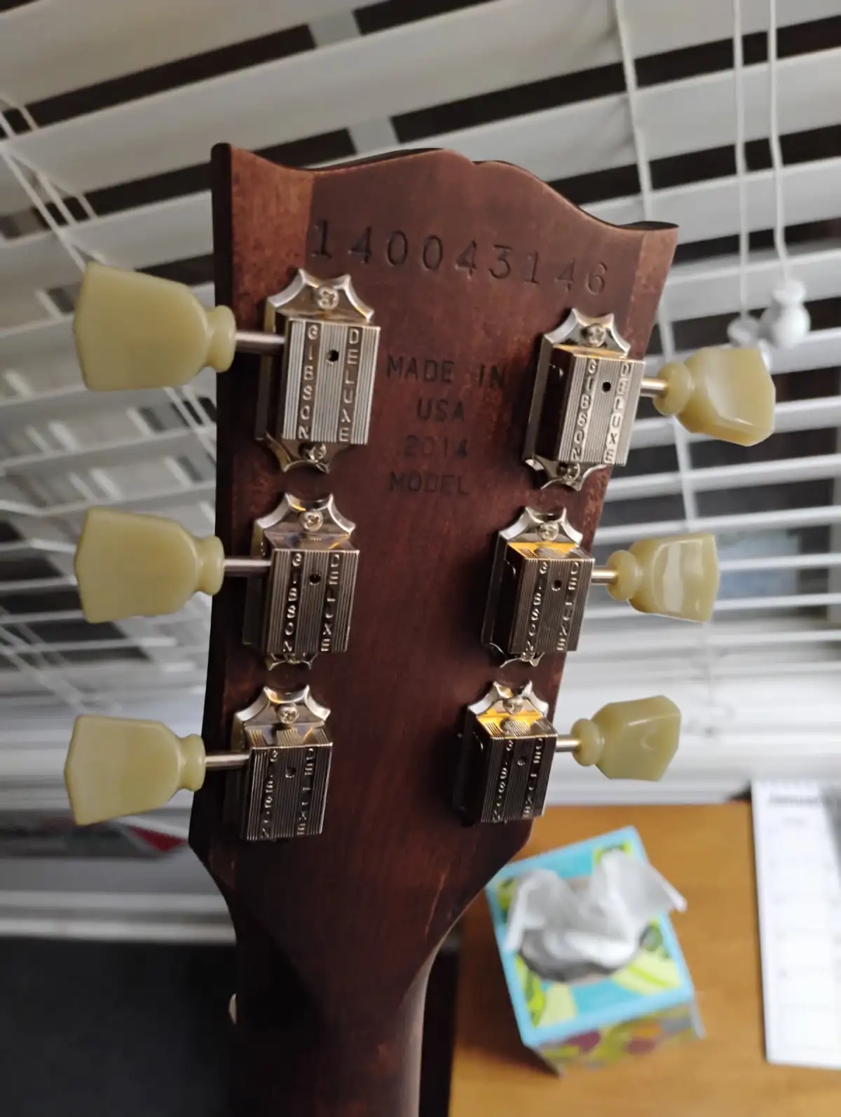 A close-up photo of a Gibson Deluxe guitar headstock showing the serial number 140043146, 'MADE IN USA 2014 MODEL' text, and…