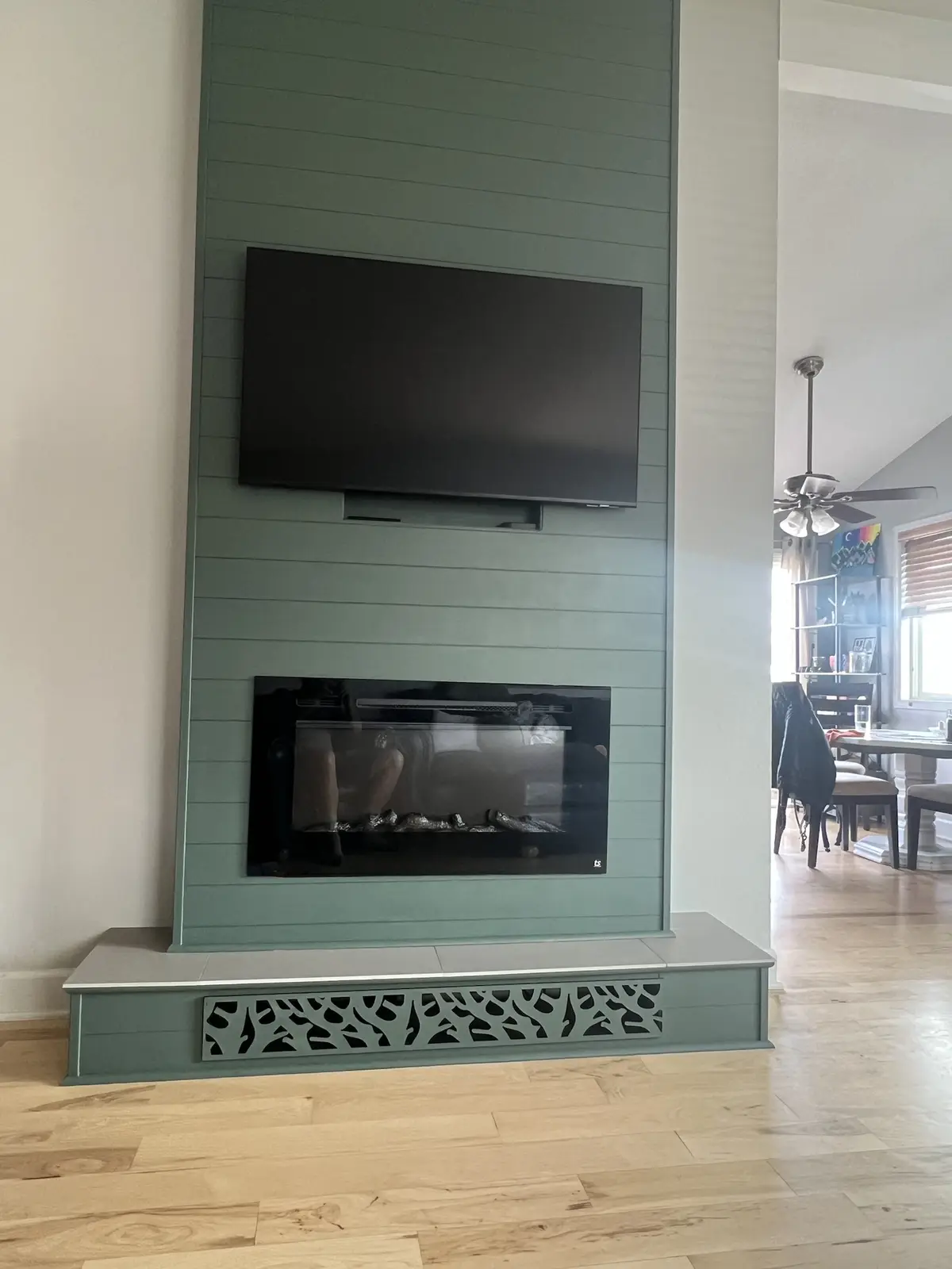 A modern living room features a teal-colored fireplace with a black glass front, mounted directly above it is a large…