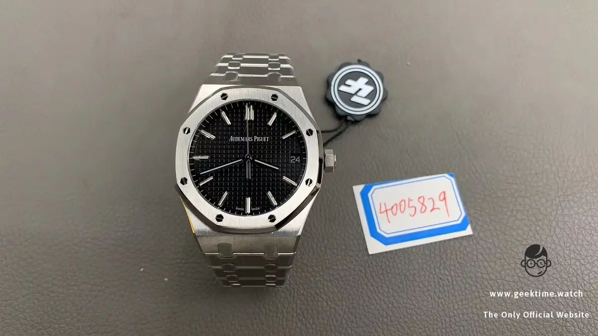 A silver Audemars Piguet Royal Oak watch with a black dial and integrated bracelet rests on a gray textured surface, next to…