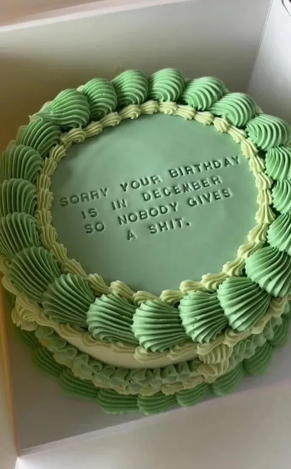 A round birthday cake with green and light green frosting piped in a decorative border around the edge. The center of the…