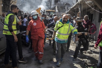 A photo shows emergency responders, including a person in a red Red Cross uniform and others in yellow safety vests…