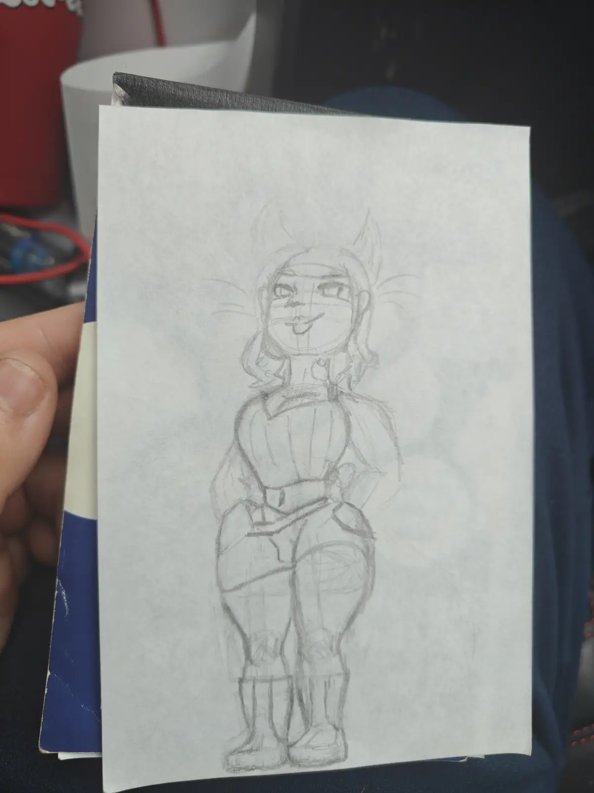 A hand holds a piece of paper with a rough pencil sketch of an anime-style female character with cat ears and a confident…