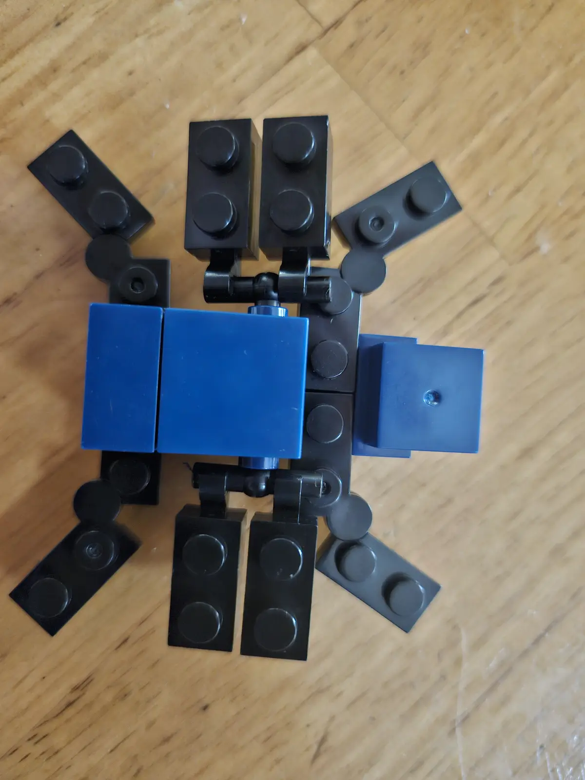 A top-down photo of a crude robot figure made from black and blue lego bricks arranged on a wooden floor, with the text 'i'm…