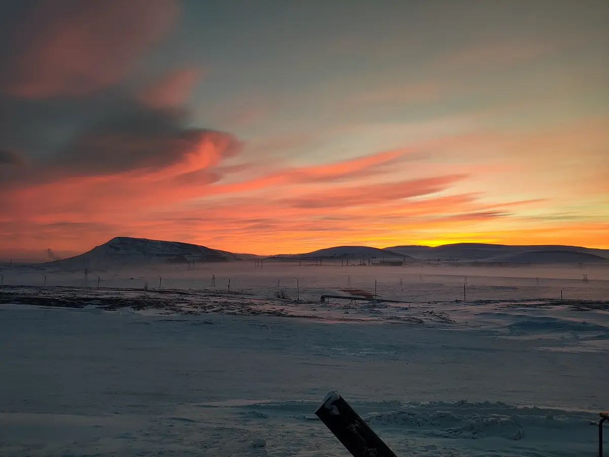 A serene, snowy landscape at sunset with vibrant orange and pink clouds above distant hills, overlaid with the text 'i'm not…