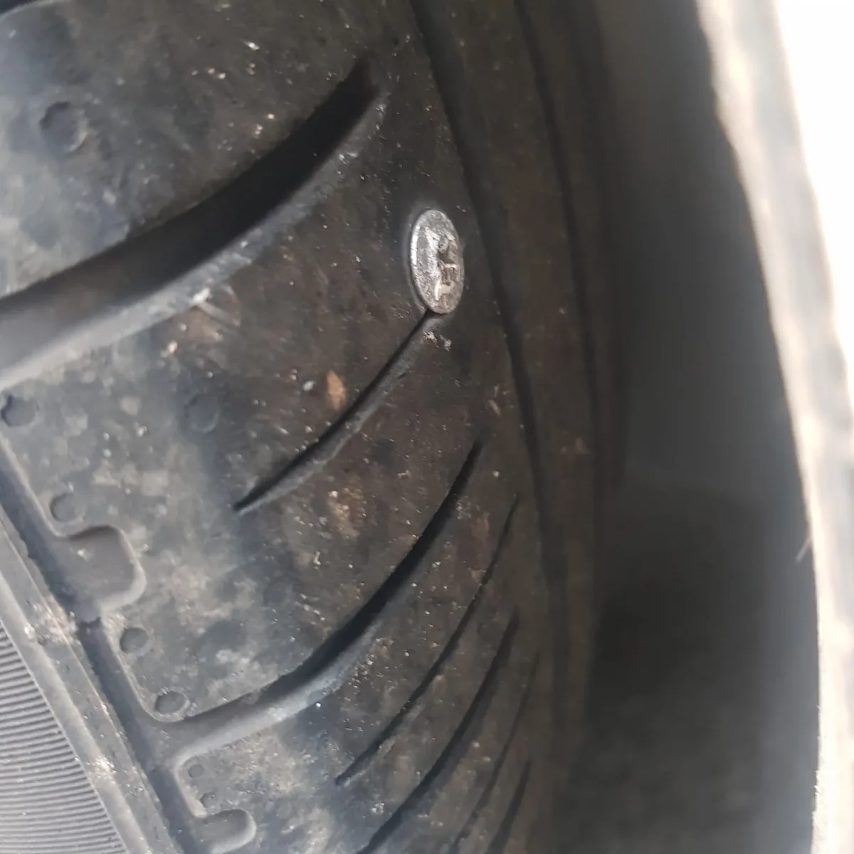 A close-up photo shows a worn, dirty black car tire tread with a single, slightly tarnished penny embedded in the rubber…