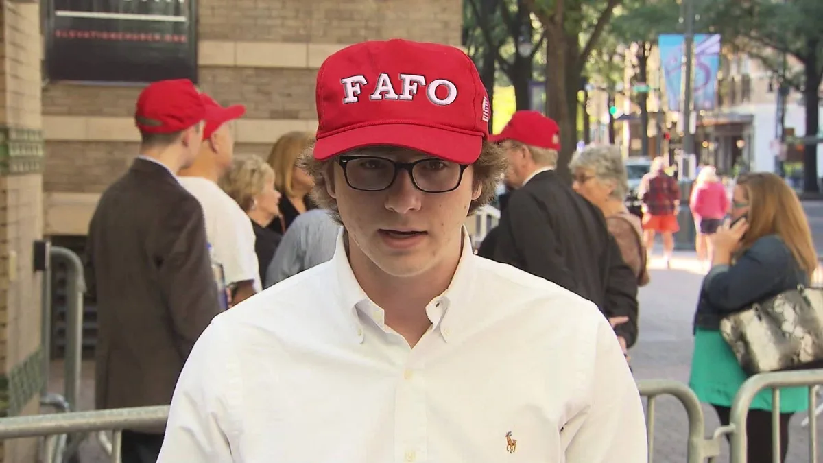 A young man with glasses and a white button-down shirt wears a red baseball cap with the letters 'FAFO' in white. He is…