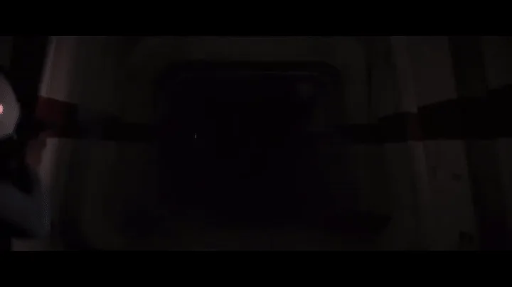 The image shows a dark, narrow corridor with a figure in a black hooded robe holding a glowing red lightsaber. The scene is…
