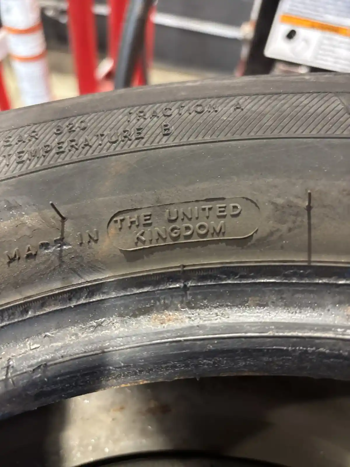 A close-up photo of a worn black car tire sidewall showing embossed text including 'MADE IN THE UNITED KINGDOM' and…