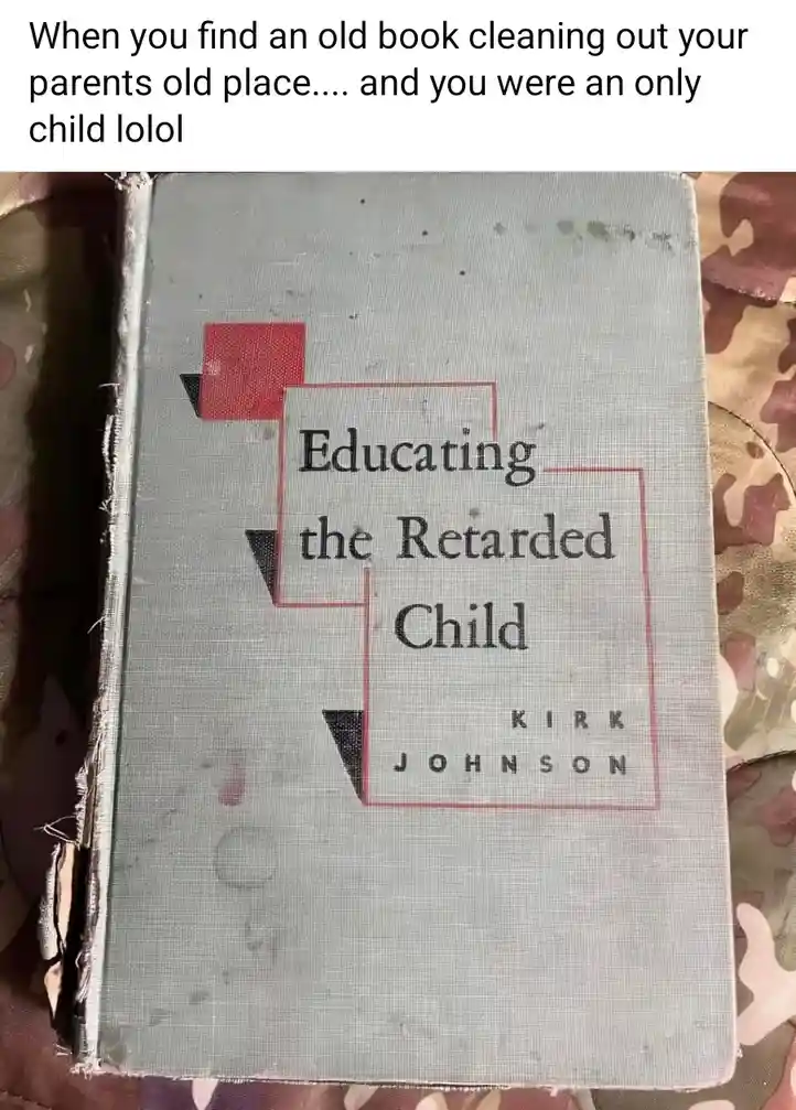 A worn, light gray book with a red and black geometric design on its cover lies on a camouflage-patterned surface. The title…