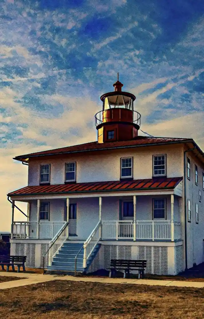 A picturesque lighthouse building with a white exterior, red roof, and a copper-colored lantern room atop, set against a…