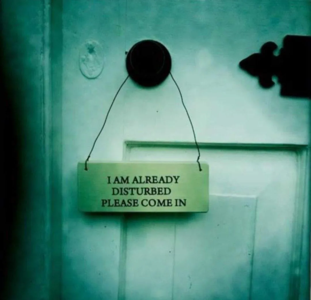 A pale green rectangular sign hangs by two black strings from a black door knob on a white door with a black metal hinge…