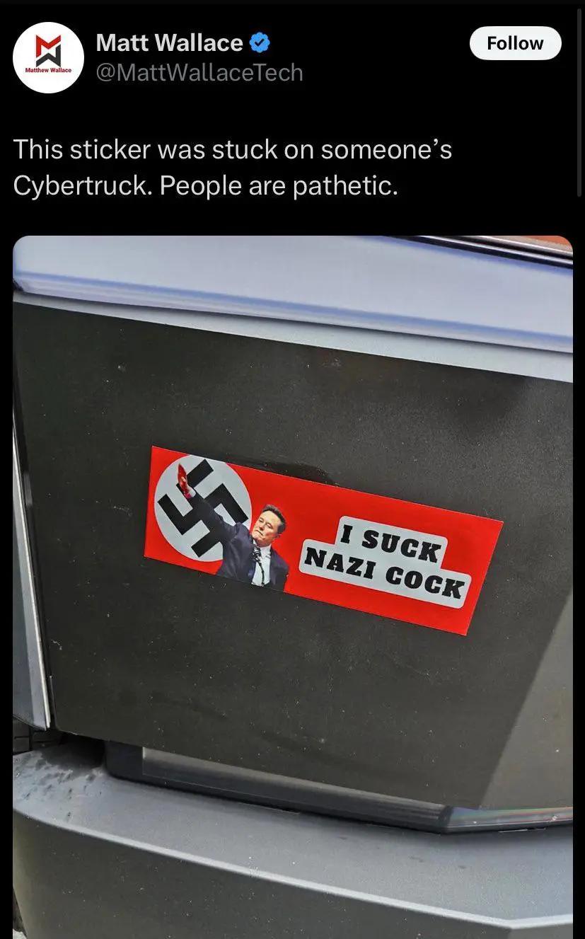 A red rectangular sticker is affixed to the black rear panel of a silver Tesla Cybertruck. The sticker features a swastika…