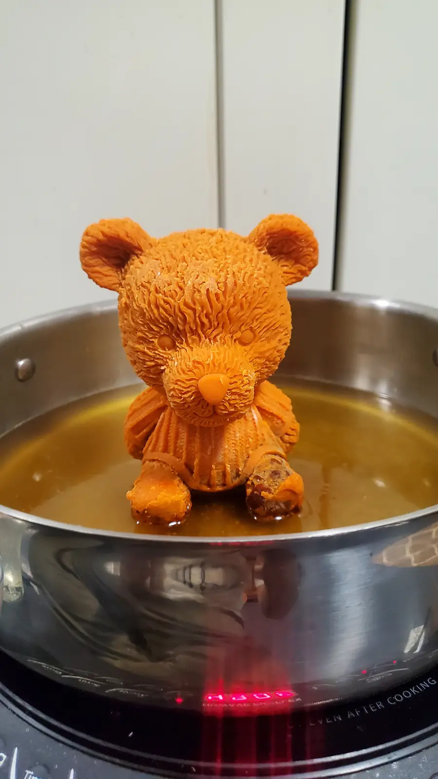 A small, orange, textured bear-shaped object, resembling a 3D-printed or carved carrot, sits upright in a stainless steel…