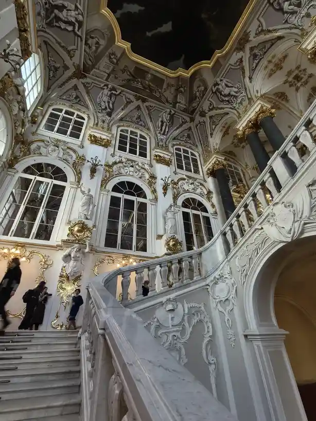A grand, ornate baroque interior with a sweeping marble staircase, gilded decorations, and numerous statues, overlaid with…