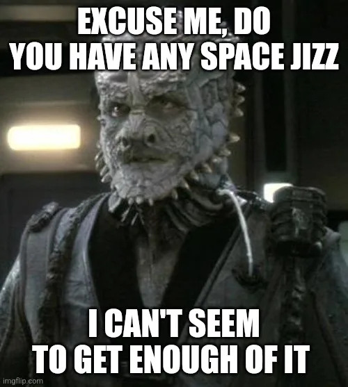 A close-up of a grey-skinned, reptilian alien with spiky facial features and a stern expression, wearing dark armor. The…