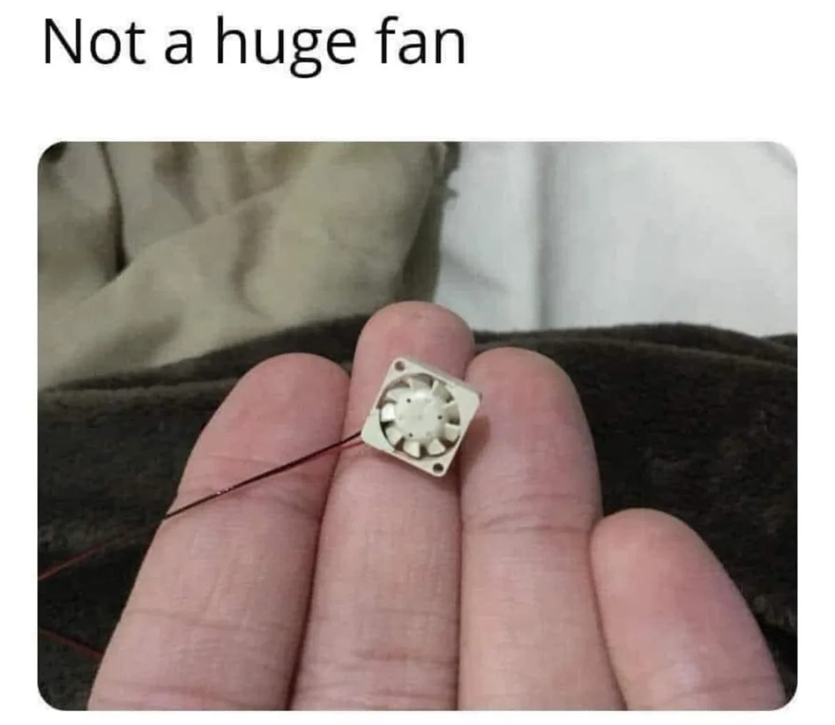A close-up photo shows a person's hand holding a tiny, square-shaped electronic cooling fan, which is significantly smaller…