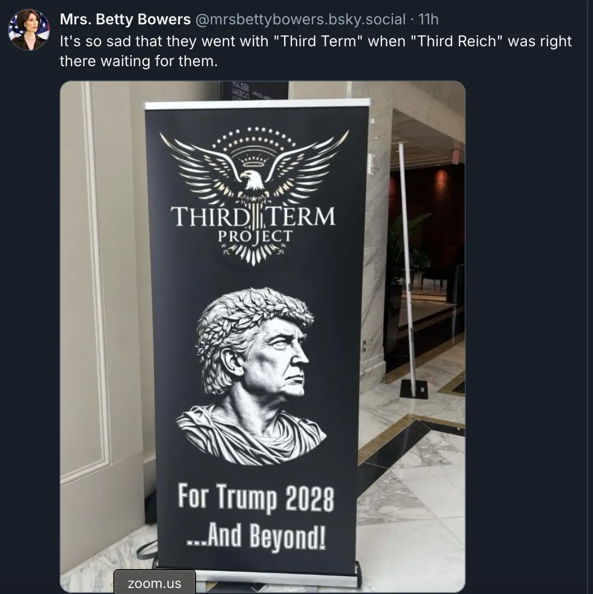 A black banner stands indoors, featuring a white emblem of an eagle with outstretched wings above the text 'THIRD TERM…