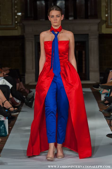 A female model walks down a runway in a striking red and blue outfit that resembles a superhero costume, with a red cape and…