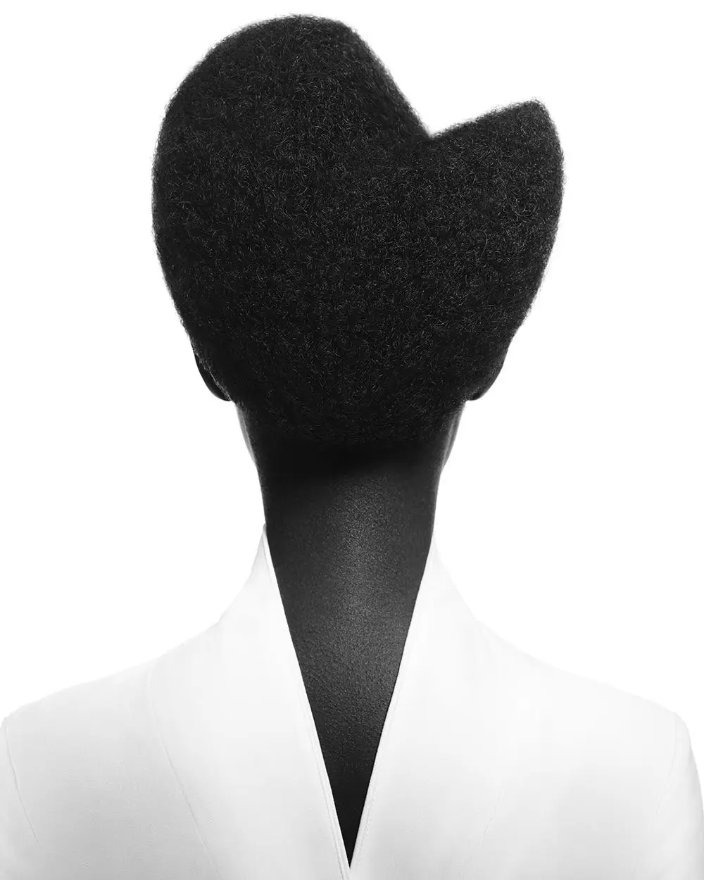 A black-and-white photo shows the back of a person with a voluminous, textured afro hairstyle that is unmistakably shaped…