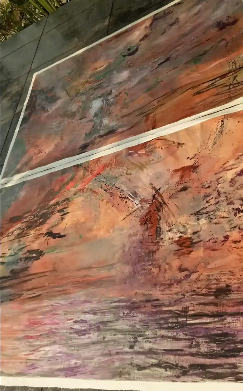 Two large abstract paintings with swirling brushstrokes in earthy tones of orange, brown, purple, and black are taped to a…