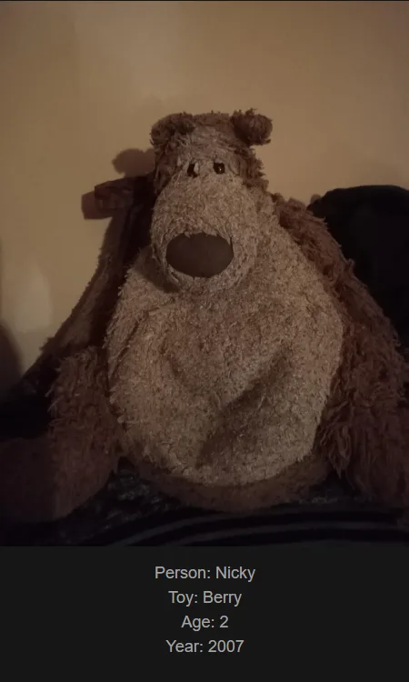A close-up photo of a worn, brown, shaggy stuffed bear toy sitting on a dark surface against a plain wall. The image has a…