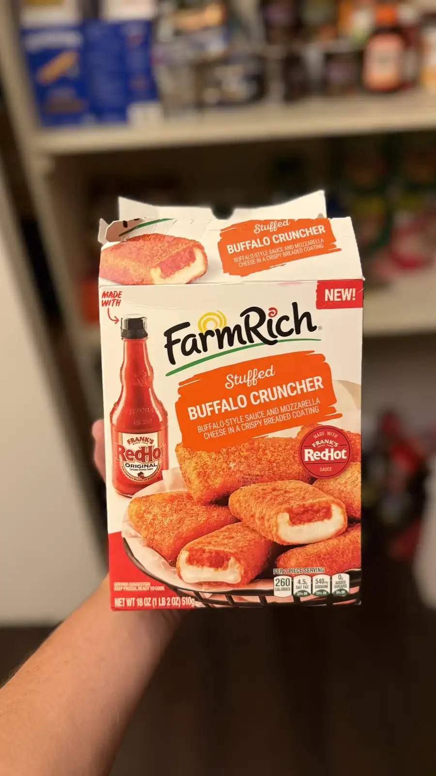 A person holds a box of Farm Rich Stuffed Buffalo Cruncher frozen appetizers, which are described as containing…