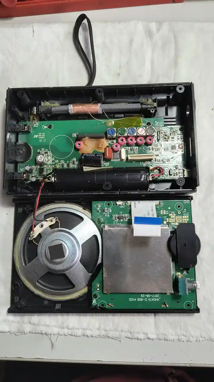 An open electronic device, likely a portable radio or player, reveals its internal green circuit boards, speaker, and…