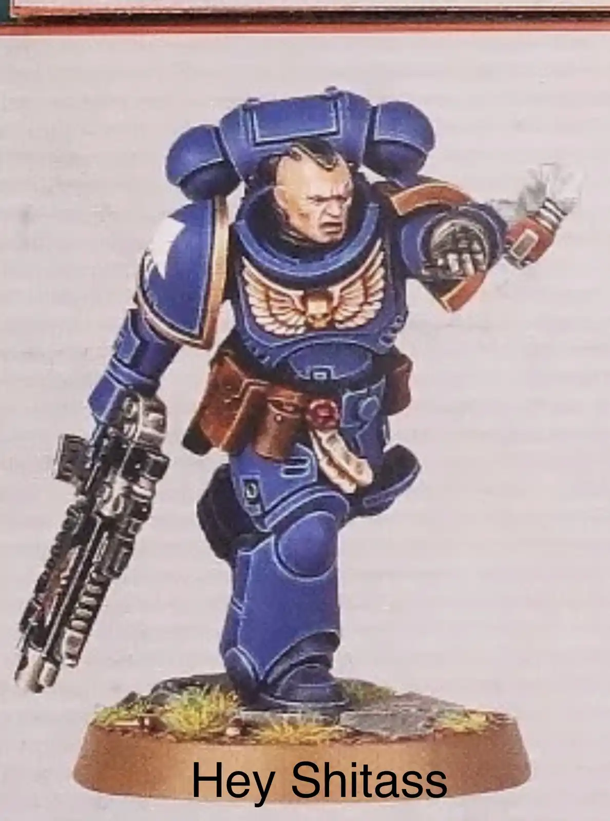 A painted miniature of a blue-armored Space Marine from Warhammer 40,000, holding a weapon and gesturing aggressively, with…