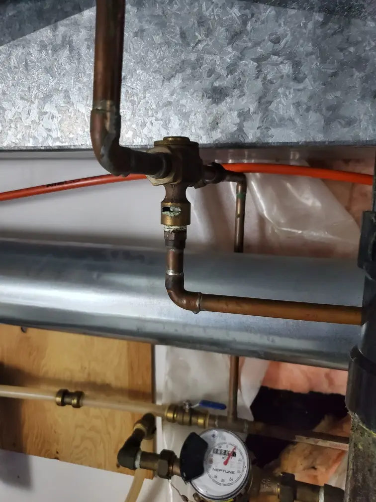 A close-up photo of copper plumbing pipes and fittings in a utility area, showing a brass valve with visible green corrosion…