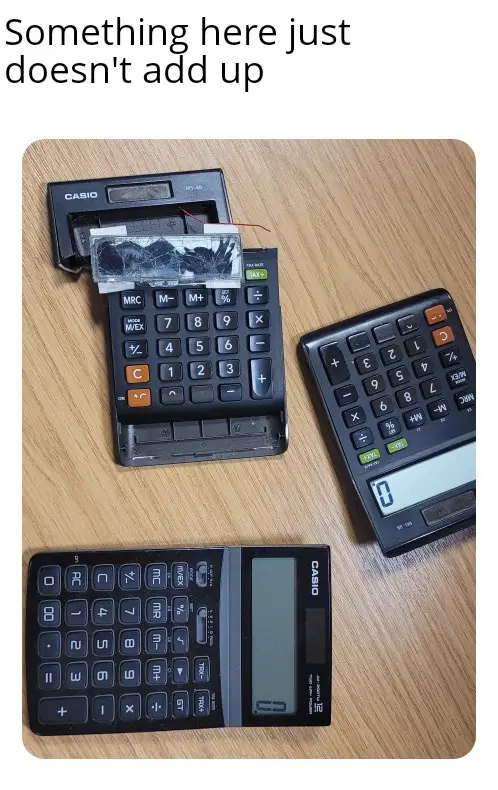 Three Casio calculators are arranged on a wooden surface; one is open with its internal circuitry exposed and taped…
