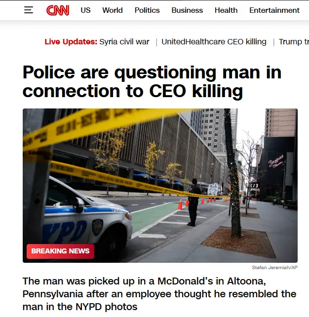 A screenshot of a CNN news article shows a police car and yellow crime scene tape on a city street, with a police officer…