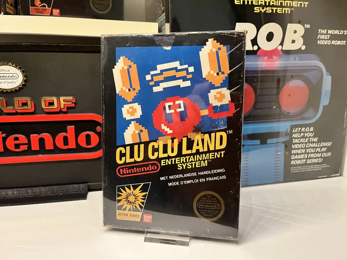 A close-up photo of a vintage Nintendo Entertainment System game box for 'Clu Clu Land', featuring pixelated orange and red…