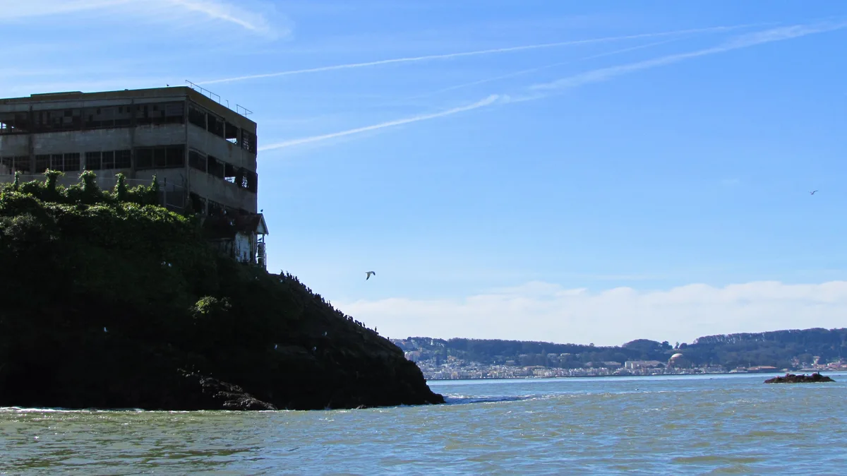 A scenic view of Alcatraz Island with its iconic, weathered prison building perched on a rocky outcrop in the bay under a…