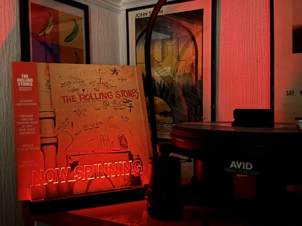 A vinyl record player with an 'AVID' brand turntable sits next to a 'The Rolling Stones' album cover that is covered in…