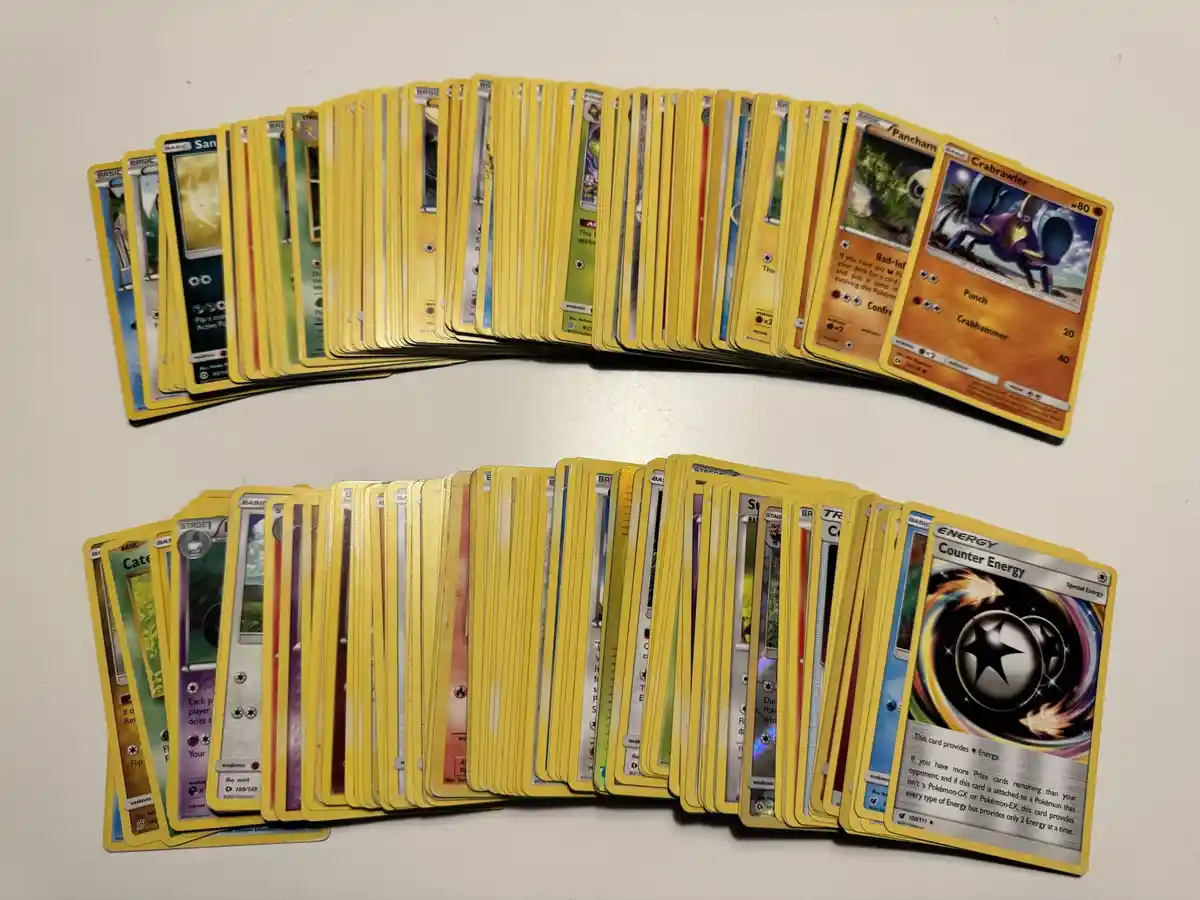 Two large fan-shaped piles of Pokémon trading cards are arranged on a white surface, with the top pile showing cards like…