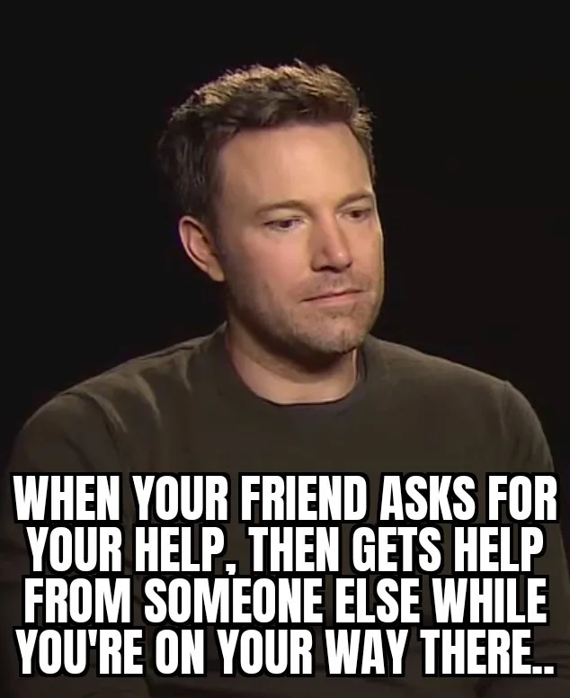 A man with short brown hair and a beard, wearing a dark t-shirt, looks down and to the side with a resigned, slightly…